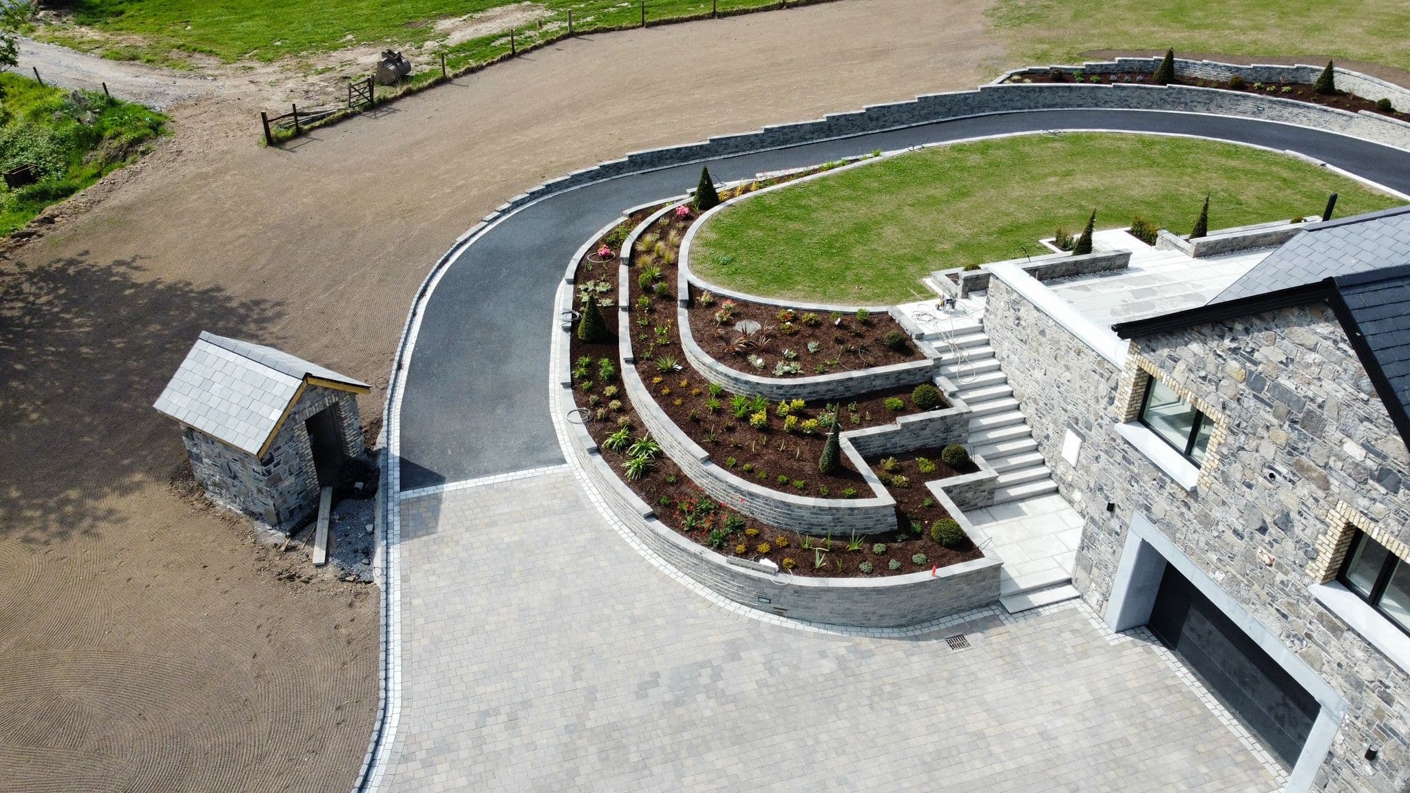 Aerial view of a finished curved granite driveway, tiered garden beds and stone house in Collinstown, Westmeath